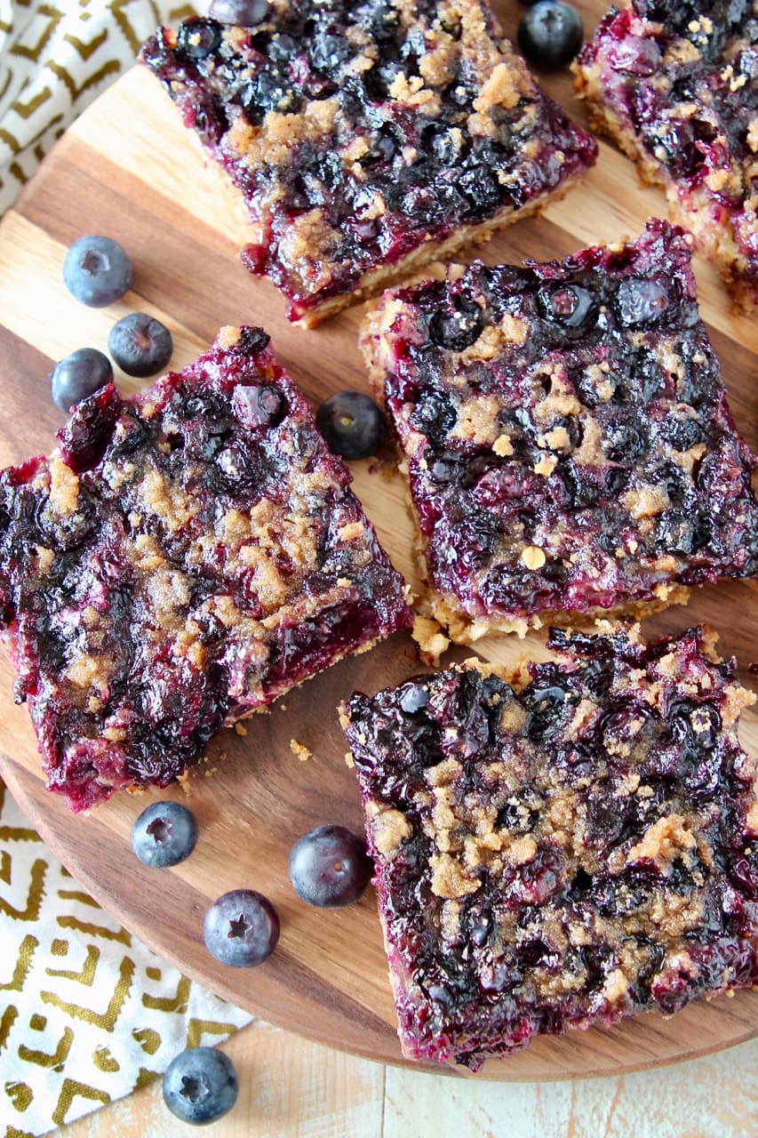 Blueberry oat bars cut into squares on wood cutting board with fresh blueberries