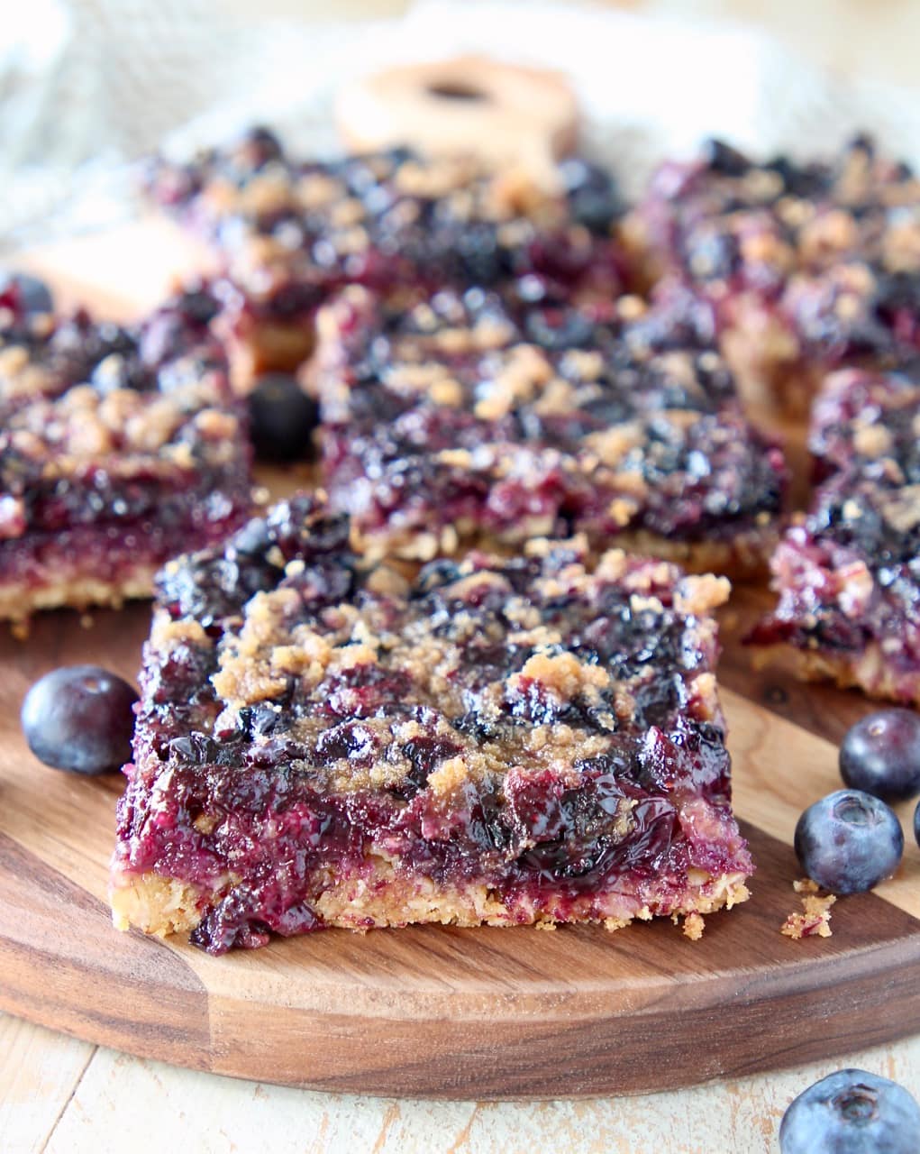 Blueberry oatmeal bars cut into squares, sitting on wood cutting board with fresh blueberries