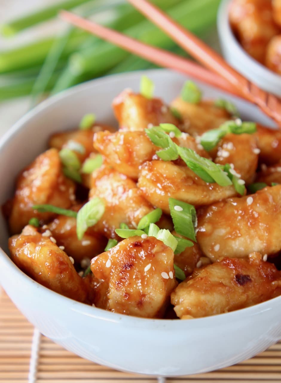 orange chicken in bowl with diced scallions and chopsticks