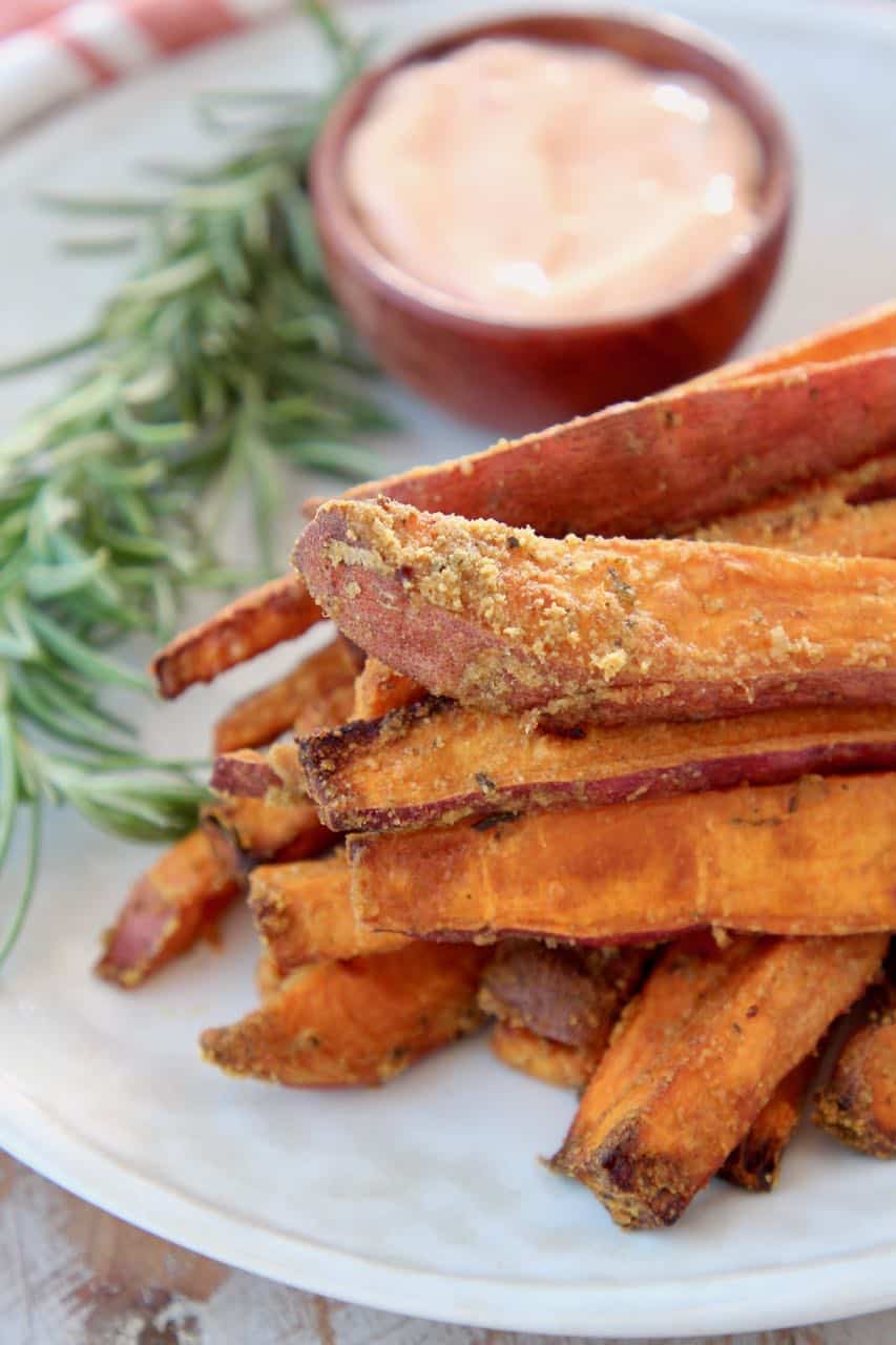 Sweet potato fries stacked up on plate with fresh rosemary sprig on the side