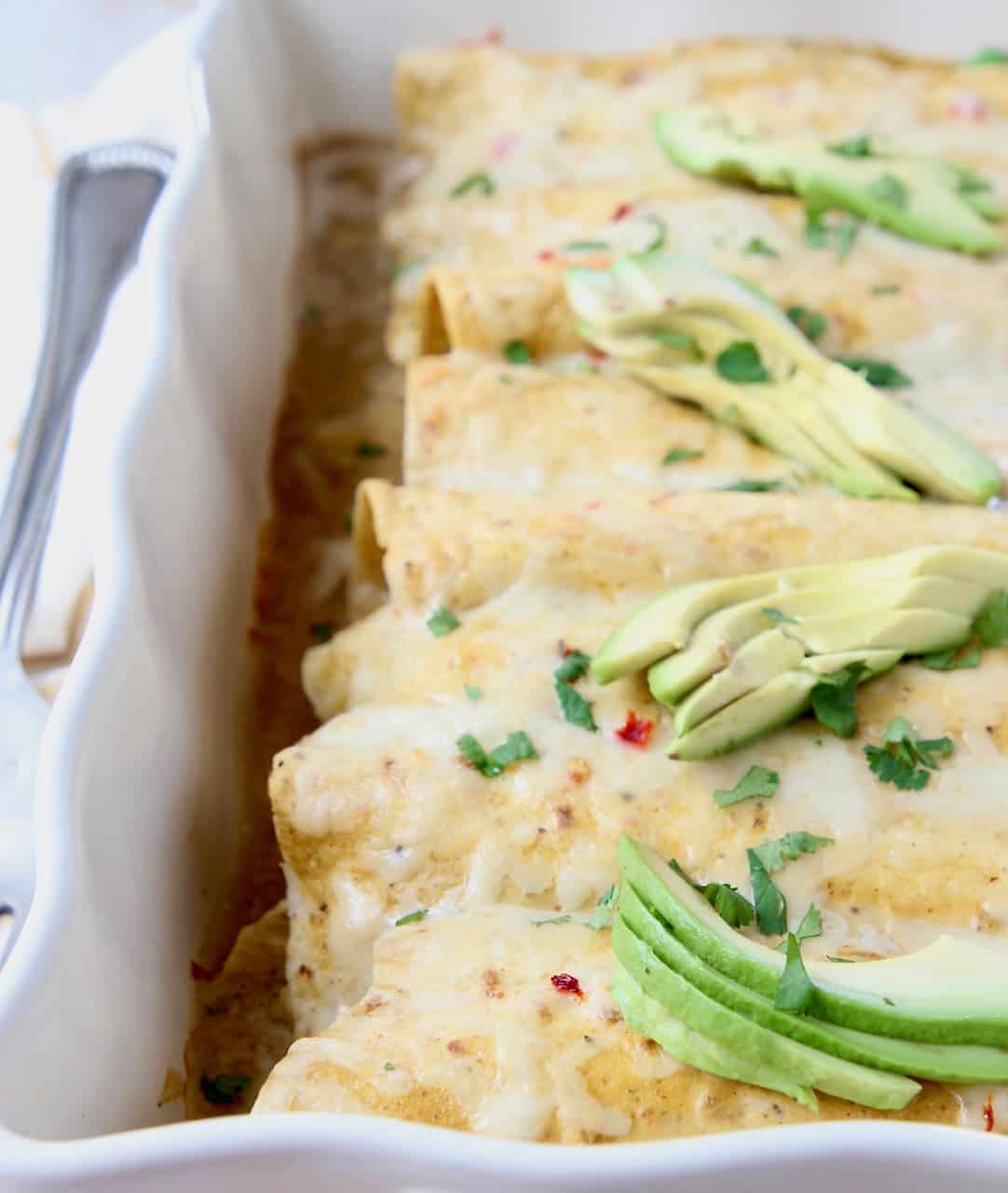 Enchiladas in baking dish topped with sliced avocados