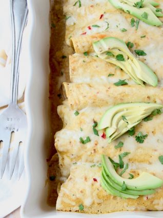 Overhead image of enchiladas with green sauce in casserole dish, topped with sliced avocado