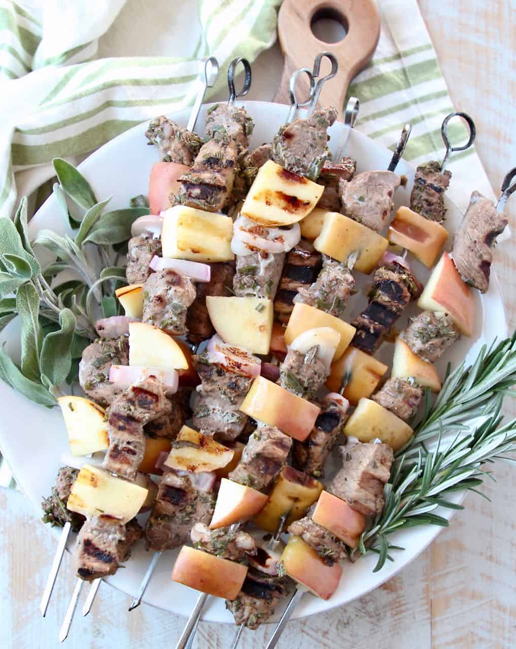 Pork skewers stacked up on plate with fresh herbs