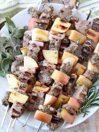 Pork and apple skewers on plate with fresh herbs
