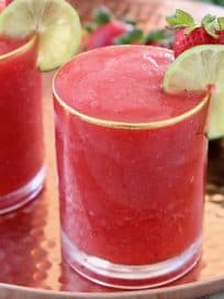 Frozen strawberry daiquiri in glass on copper tray with fresh lime wedges