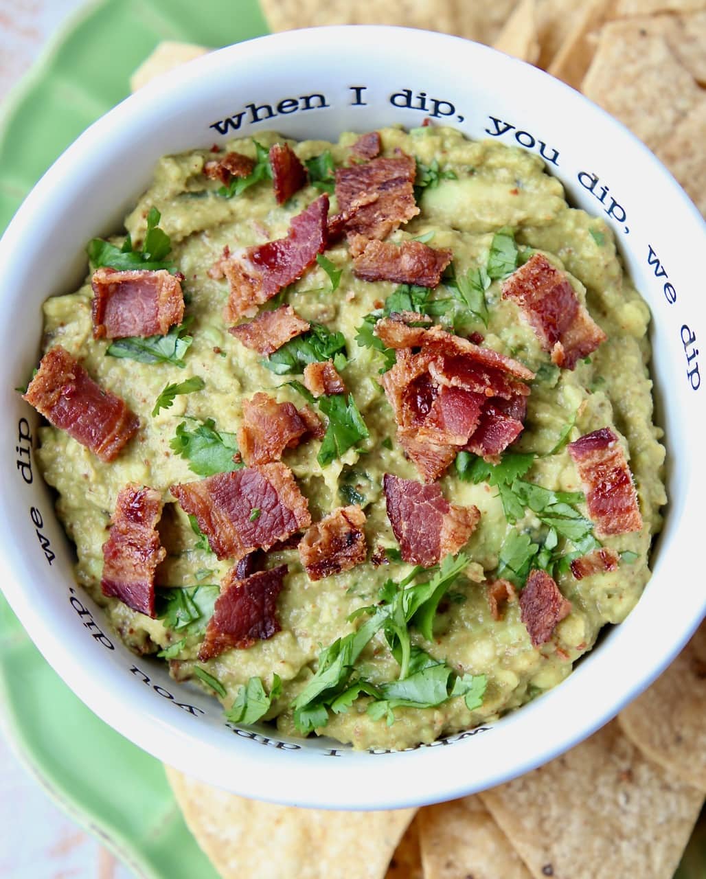 Guacamole in white bowl with crumbled cooked bacon on top