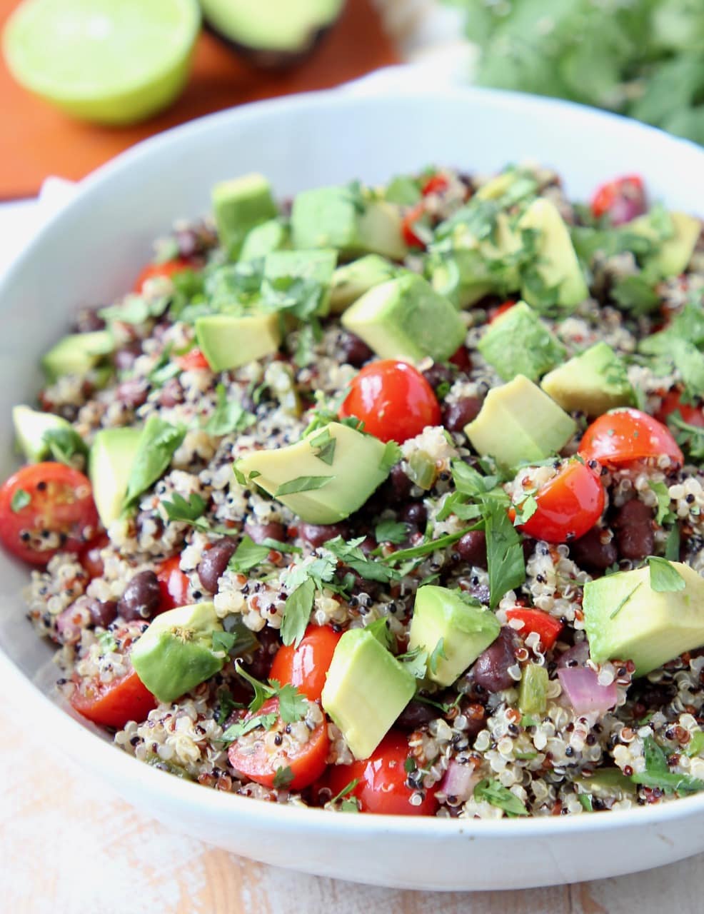 Quinoa salad in white bowl topped with diced avocado and cilantro