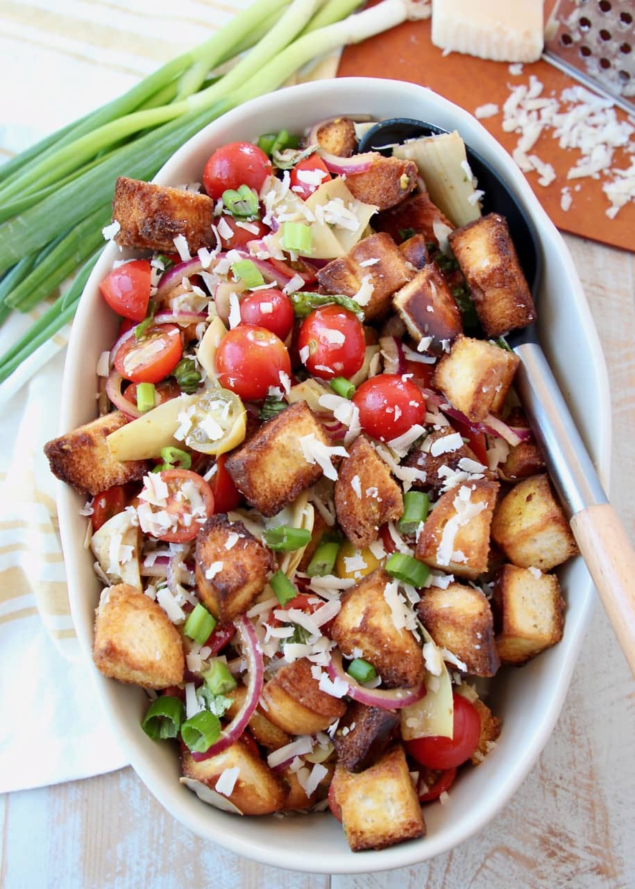 Toasted bread cubes, cherry tomatoes and parmesan cheese in large oval bowl with spoon in bowl