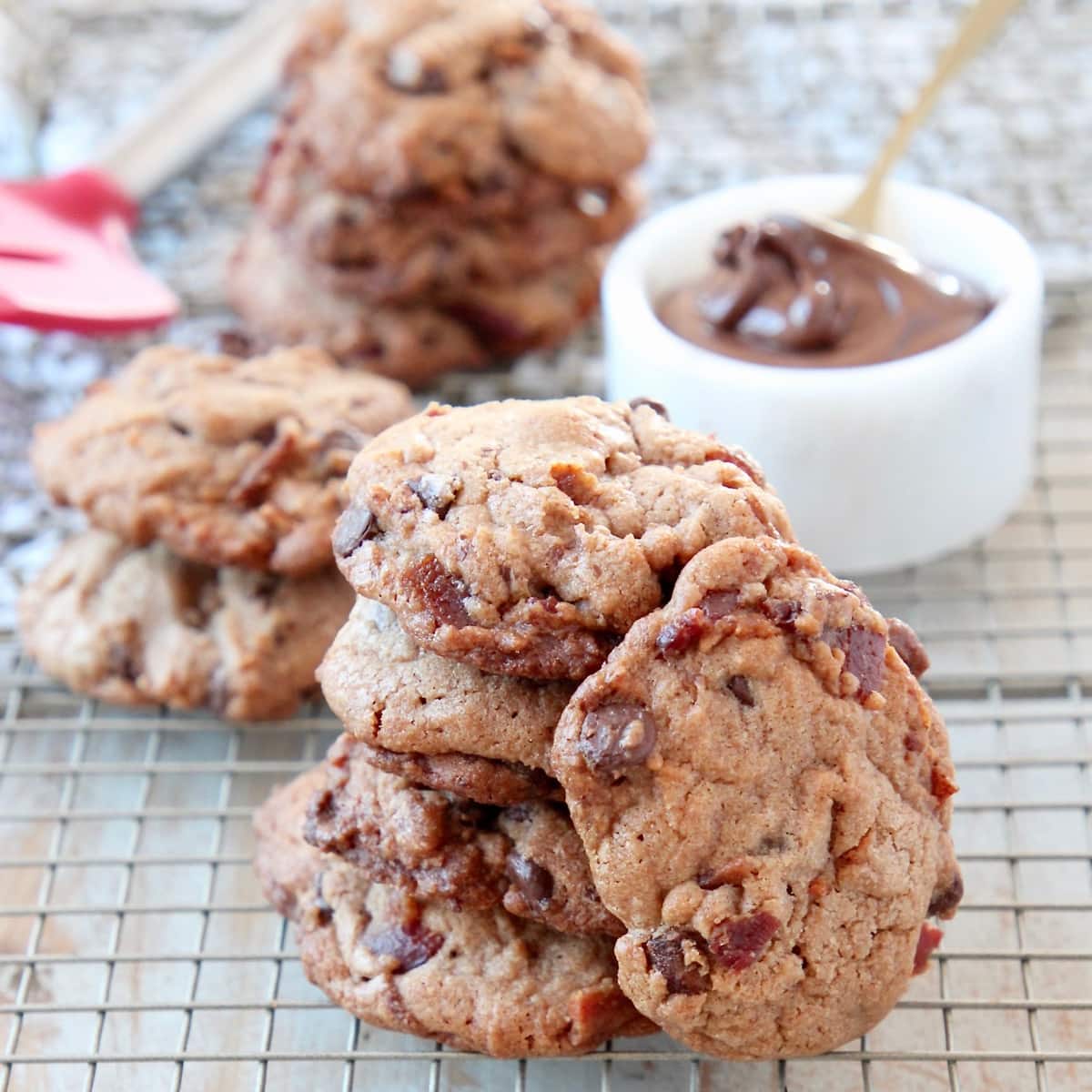 Bacon Chocolate Chip Cookies stacked up on wire baking rack with bowl of nutella
