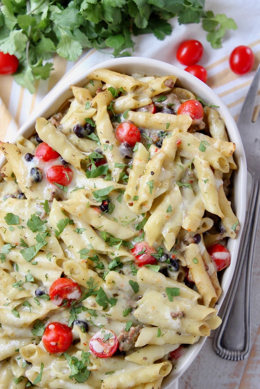 Baked taco pasta in a casserole dish with black beans, cherry tomatoes and cilantro
