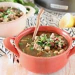 Greek turkey soup with chickpeas and spinach in orange bowl with sliced lemon