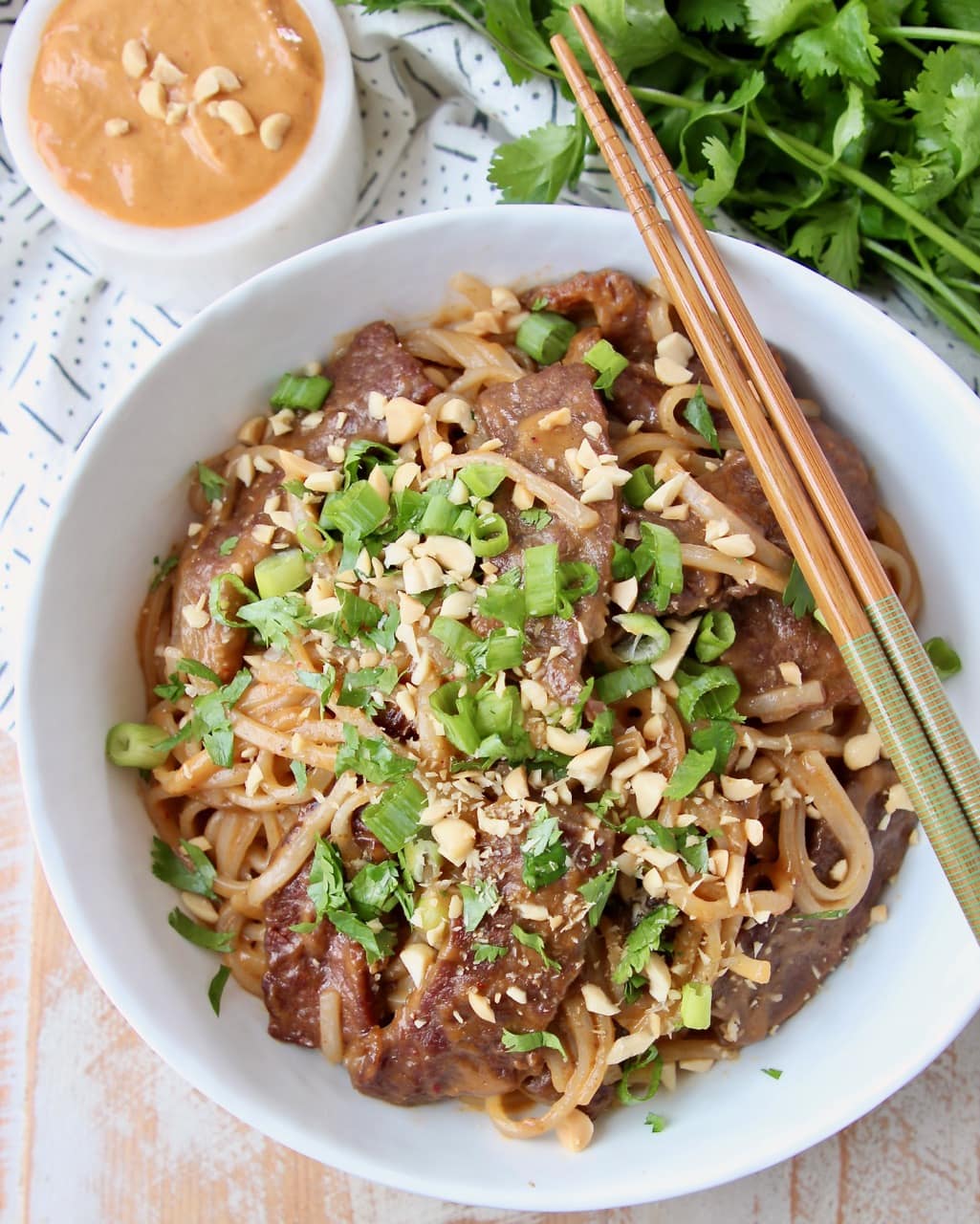 Thai beef and noodles in white bowl, topped with diced green onions