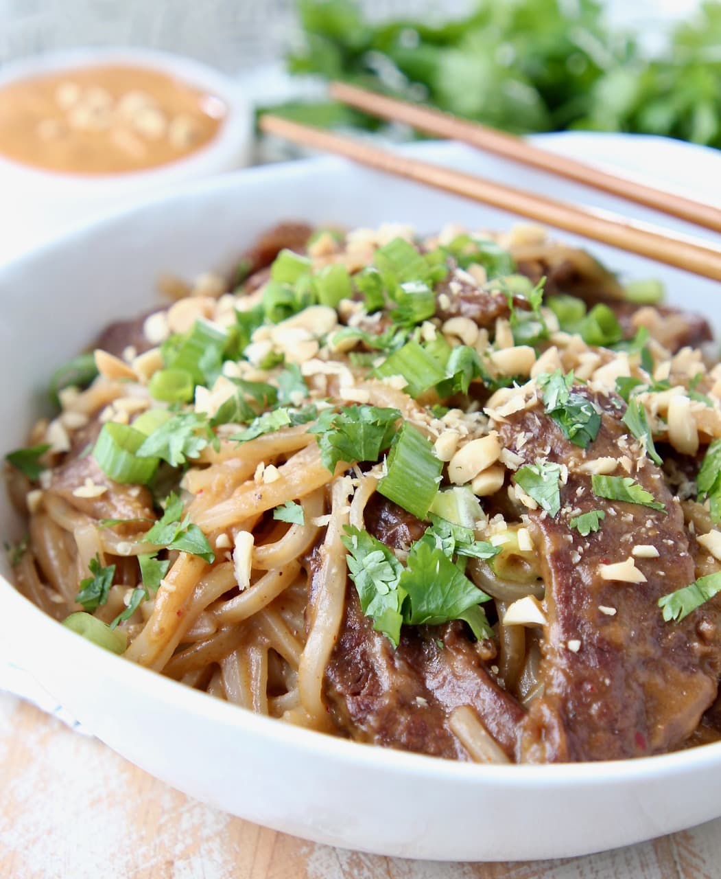 Sliced beef, noodles and sliced green onions in bowl with chopsticks on the side