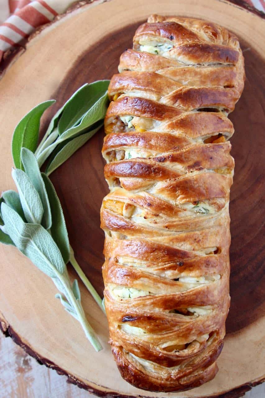 Braided puff pastry strudel on wood cutting board with fresh sage on the side