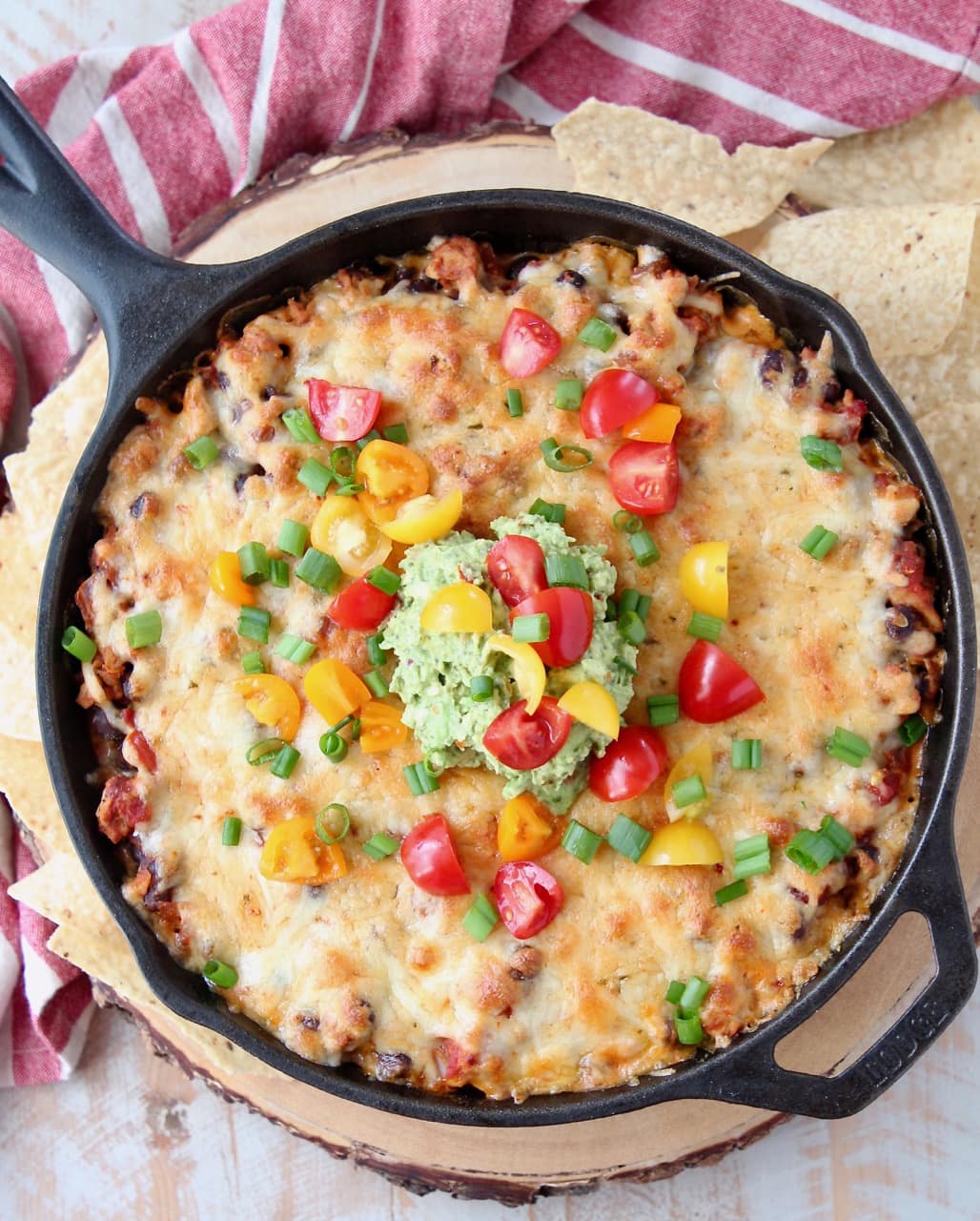 Overhead shot of cheesy taco dip baked in a cast iron skillet topped with diced cherry tomatoes and guacamole