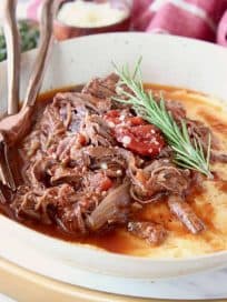 Shredded beef ragu tomato sauce in bowl with creamy polenta and rosemary sprig