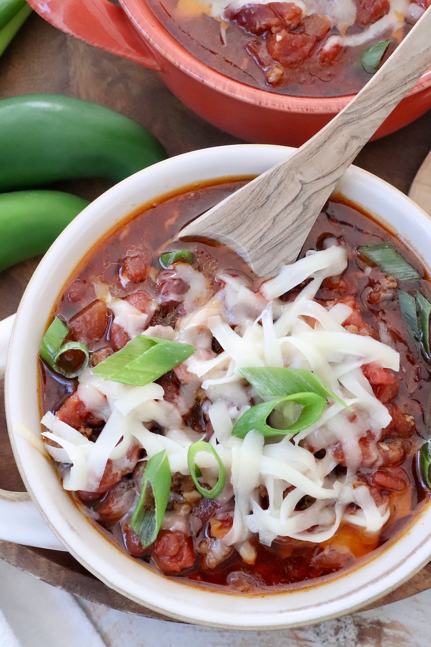 chili in a bowl topped with shredded cheese and diced green onions