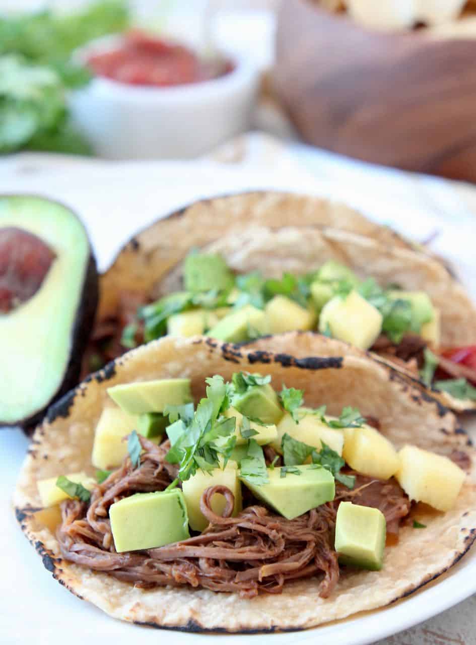 Shredded beef tacos topped with diced pineapple and avocado