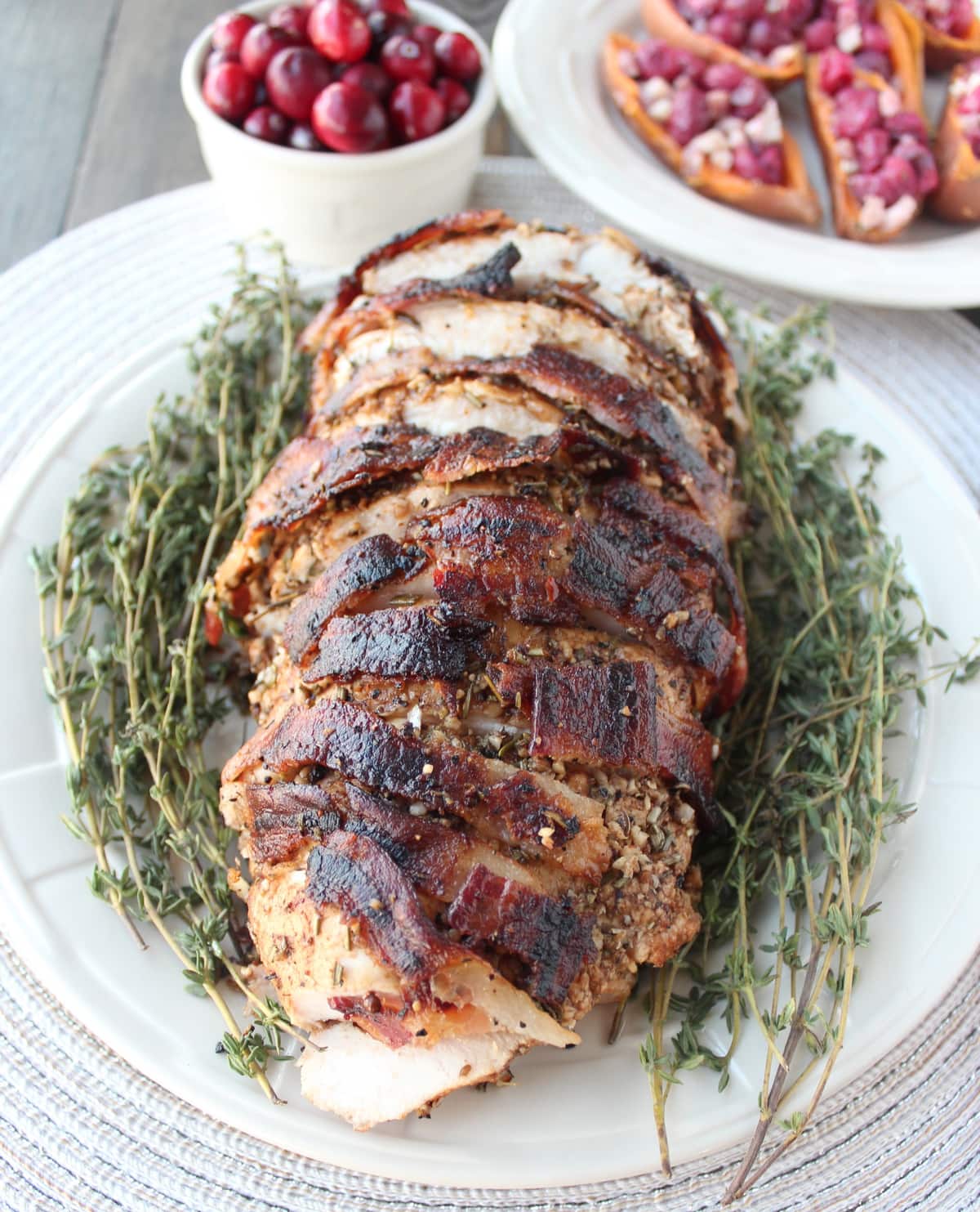 sliced, cooked bacon wrapped turkey breast on plate with fresh herbs