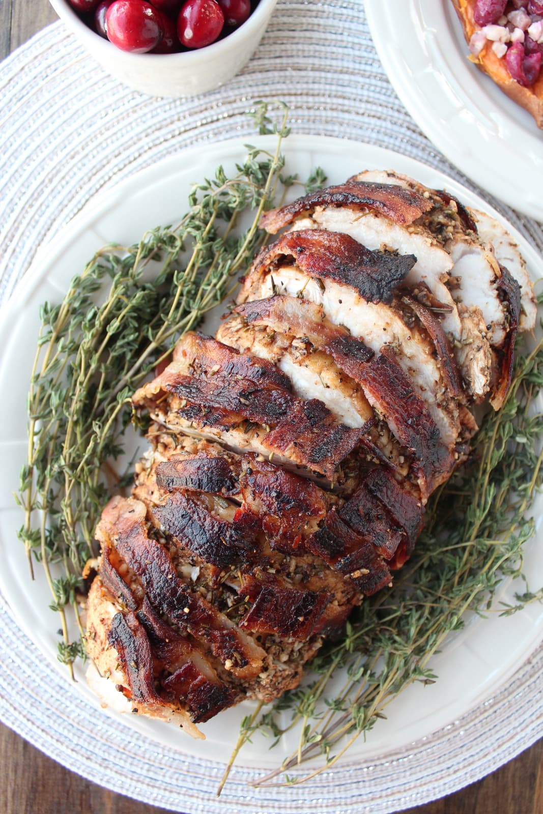 bacon wrapped turkey breast sliced on plate with fresh thyme sprigs
