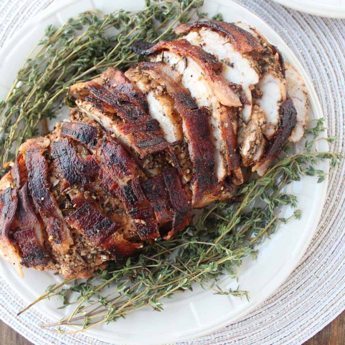 sliced, cooked bacon wrapped turkey breast on plate with fresh herbs