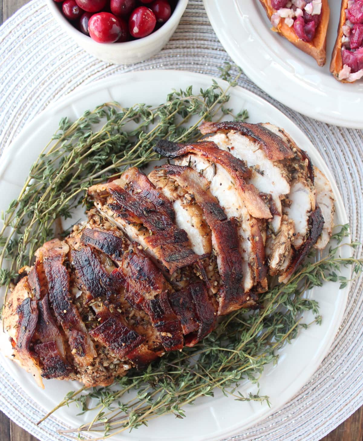 Bacon Wrapped Turkey Breast sliced on plate with fresh herbs