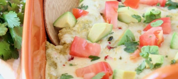 Enchilada casserole in orange baking dish with wooden spoon