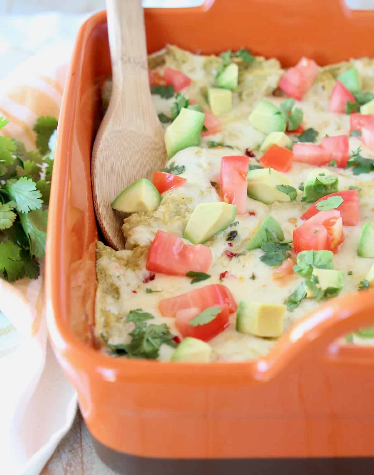 Enchilada casserole in orange baking dish with wooden spoon