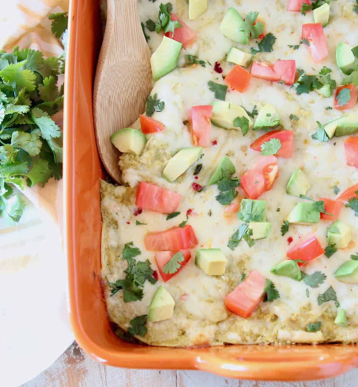 Chicken enchilada casserole topped with diced tomatoes and avocado