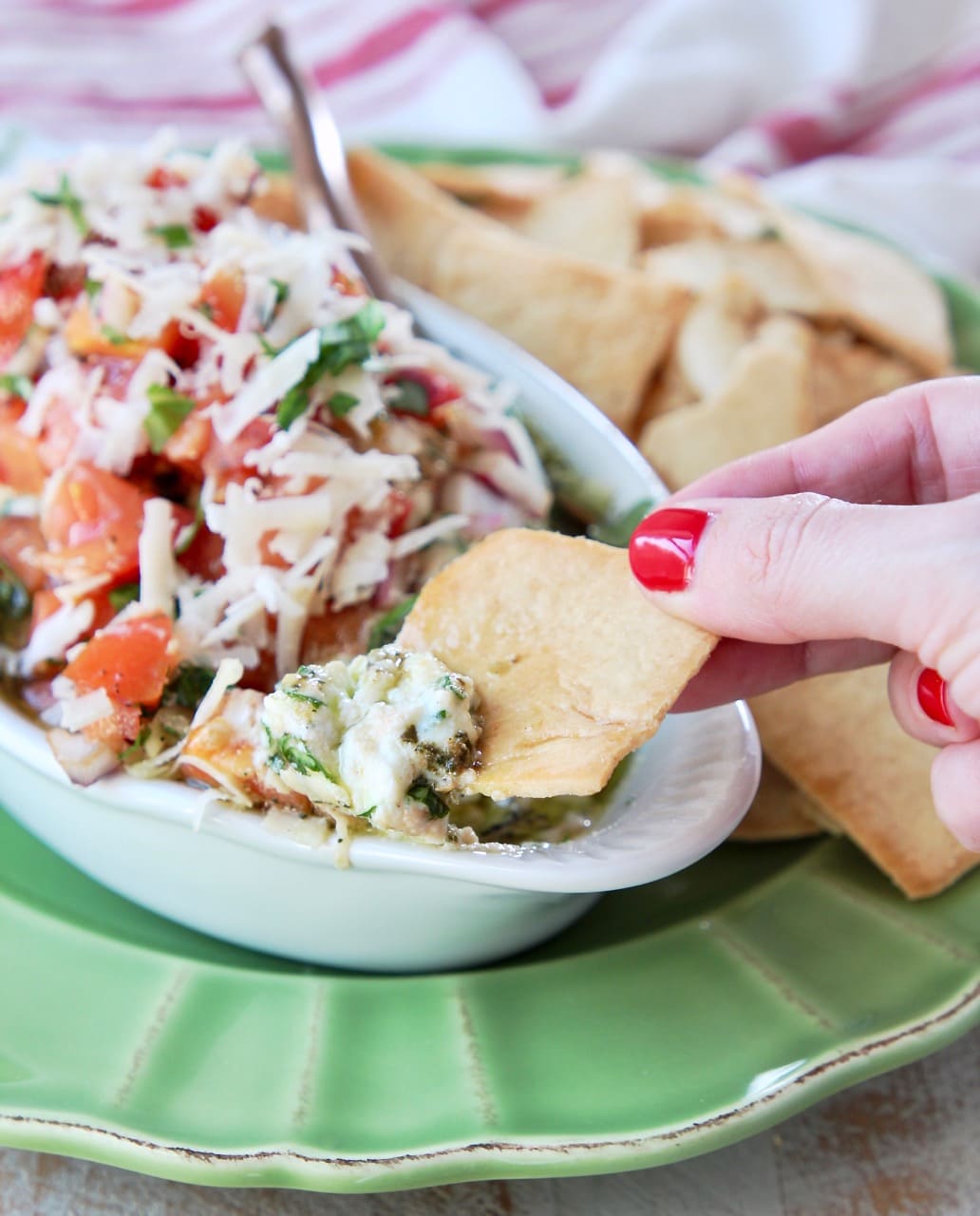 Hand dipping a pita chip into a bowl of Italian 5 layer dip