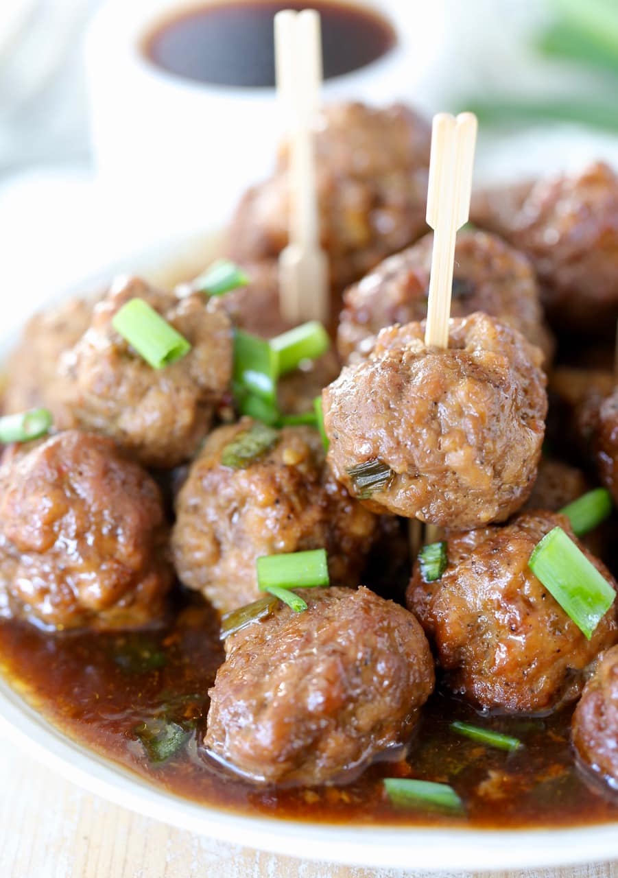 Korean BBQ meatballs piled on a plate topped with green onions with wooden skewers stuck in the meatballs