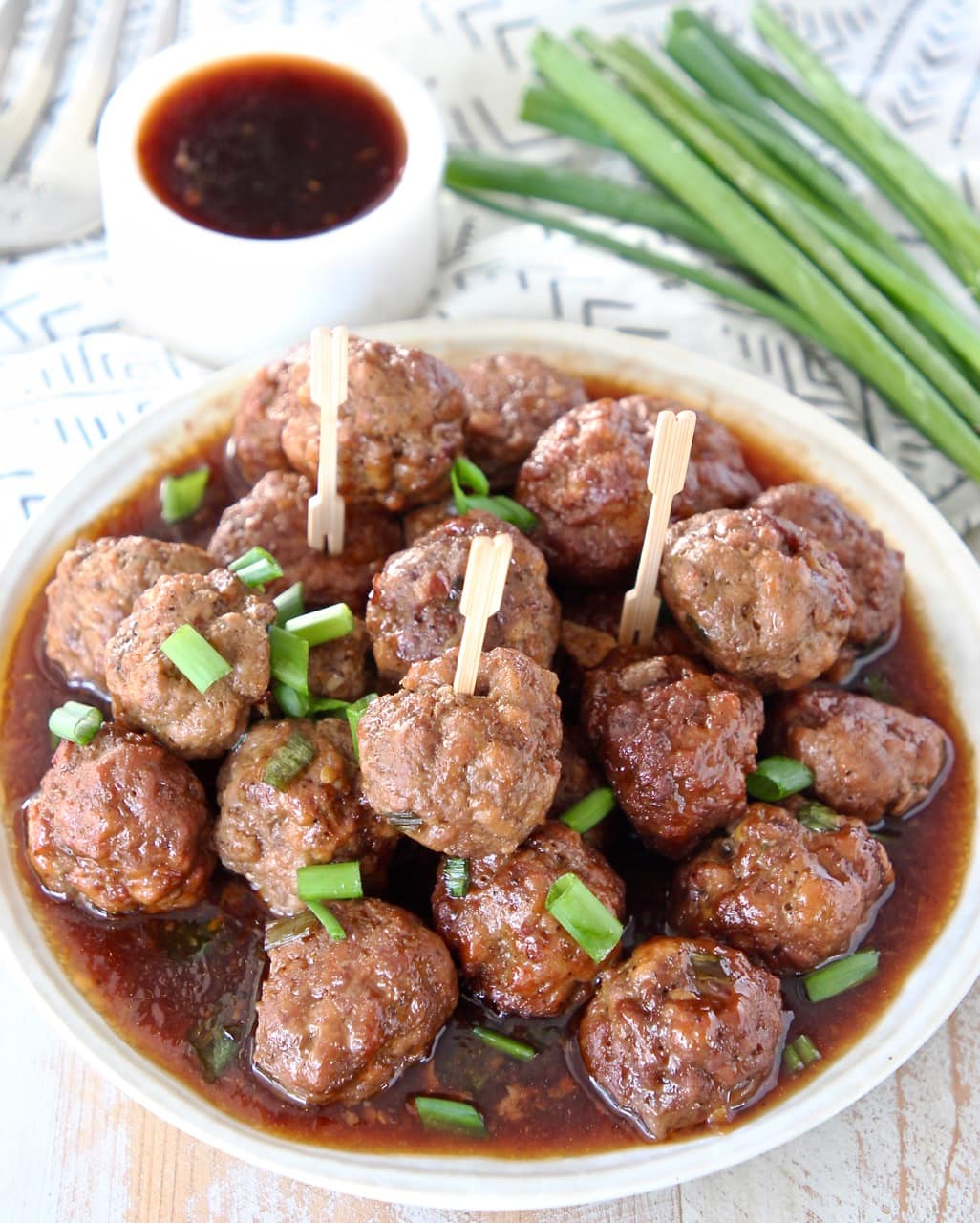 Korean BBQ meatballs on a plate with Korean bbq sauce on the side and green onions