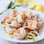 Shrimp on top of pasta on plate with gold fork swirling pasta on the side of the plate
