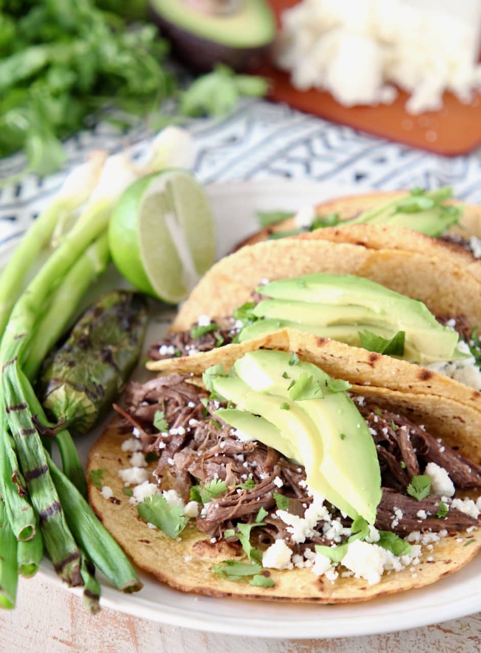 Slow Cooker Shredded Beef Barbacoa Tacos with Grilled Green Onions, Sliced Avocado, Cilantro and Cotija Cheese