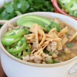 white chicken chili in bowl topped with tortilla strips and avocado slices