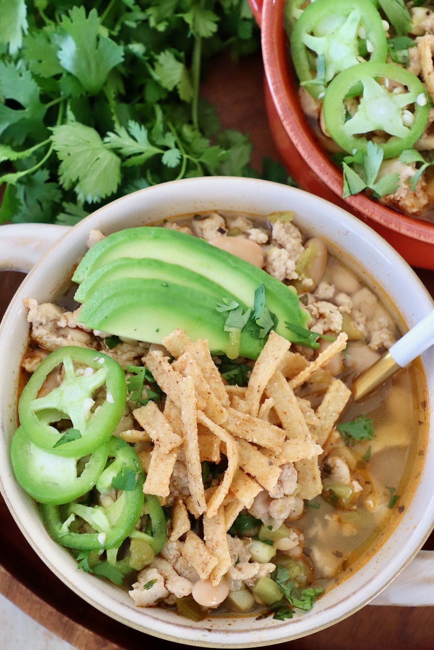 white chicken chili in bowls topped with sliced jalapenos, avocado and tortilla strips