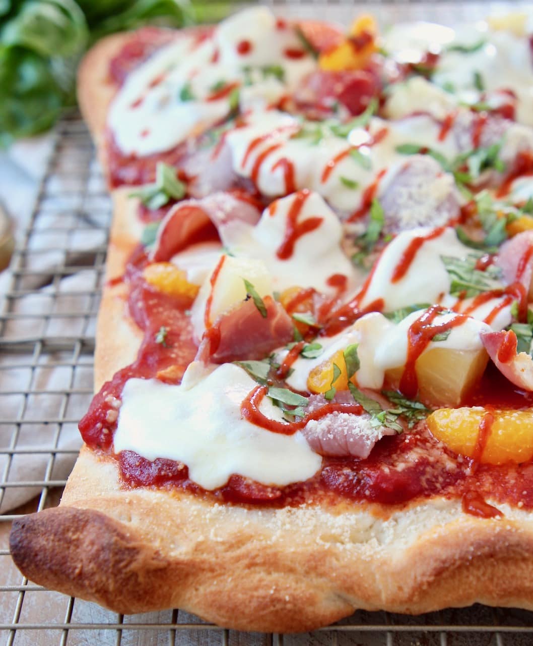 Hawaiian pizza topped with sriracha, cheese and pineapple on a wire rack