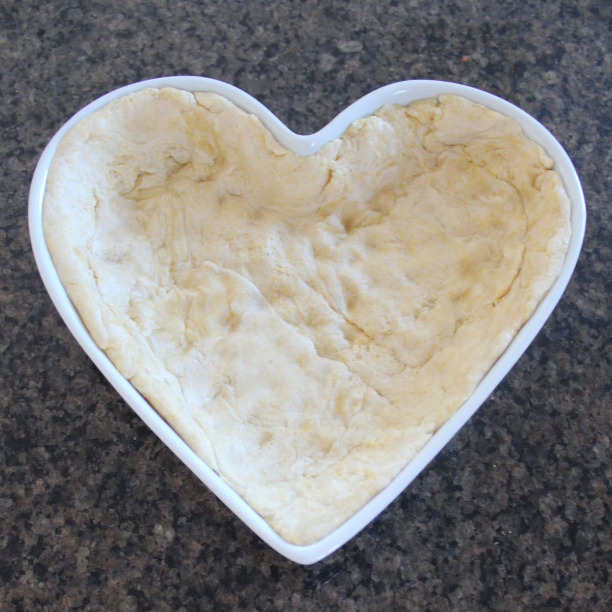 Pizza dough lining the bottom of a heart-shaped pan.
