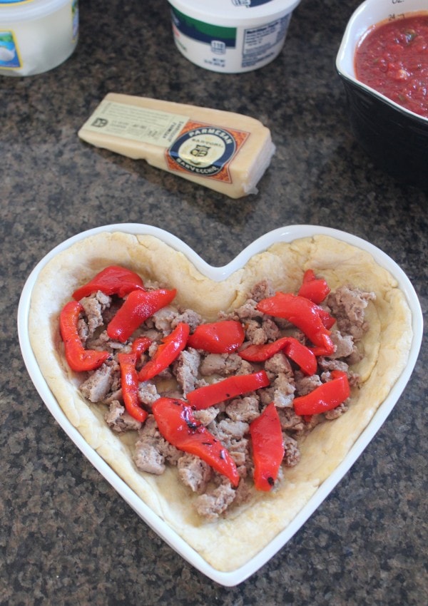Cooked sausage and roasted red peppers in heart-shaped pizza dough.