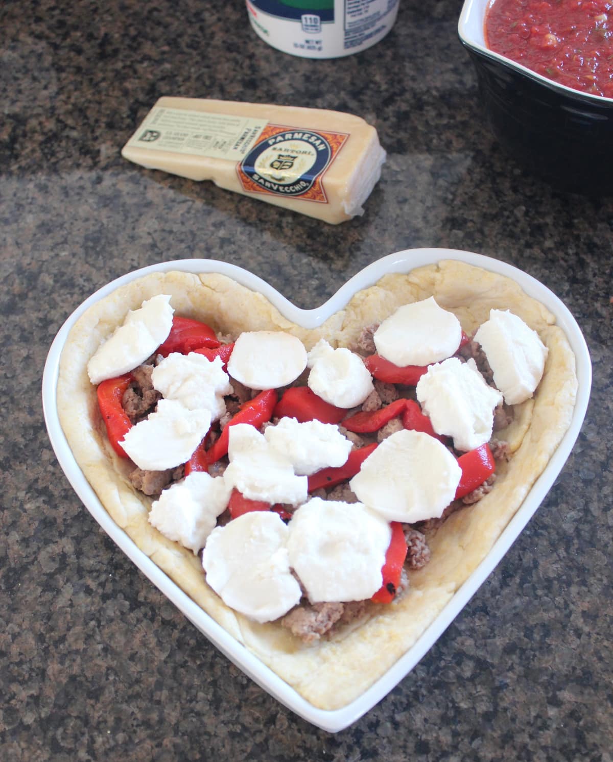 Fresh mozzarella topping sausage and peppers in a pizza shaped like a heart.
