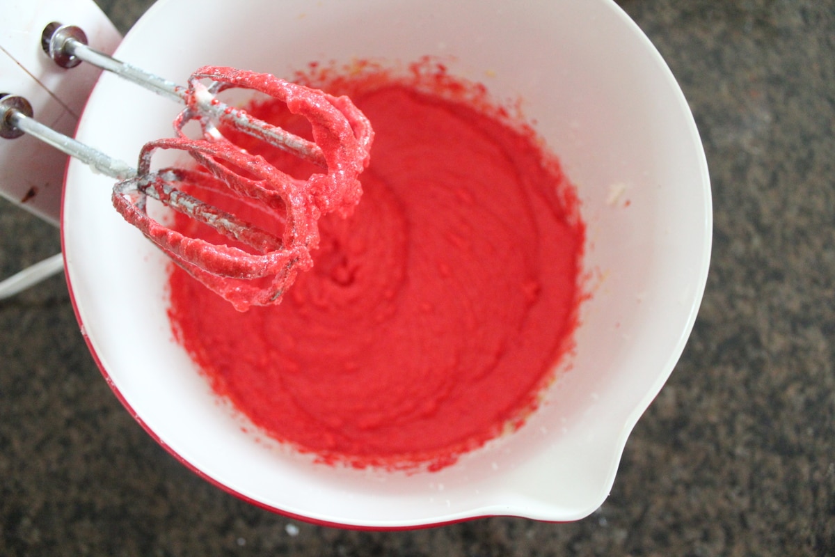 An electric mixer resting above red velvet cookie batter. 