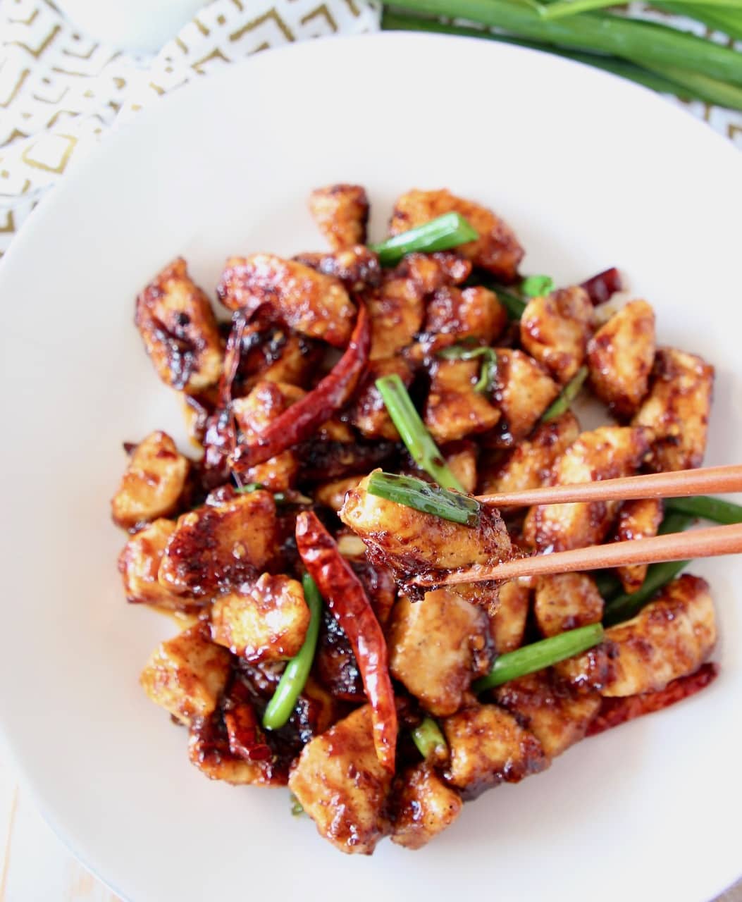 General tso chicken on a white plate with chopsticks picking up a piece of chicken