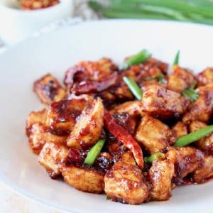 General Tso chicken with red chilies and green onions on white plate