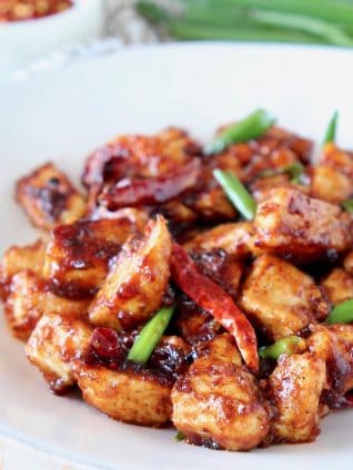 General Tso chicken with red chilies and green onions on white plate