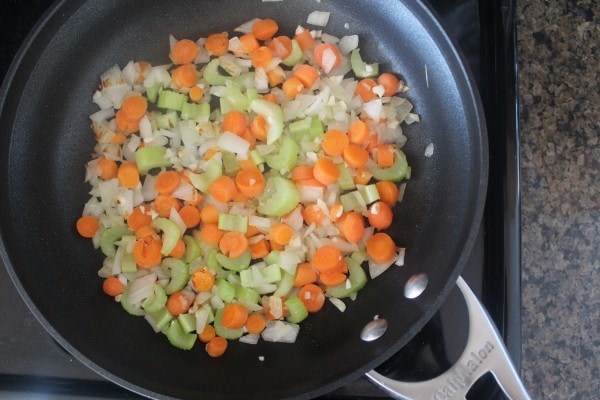 Carrots, onion, and celery sautéing in a skillet.