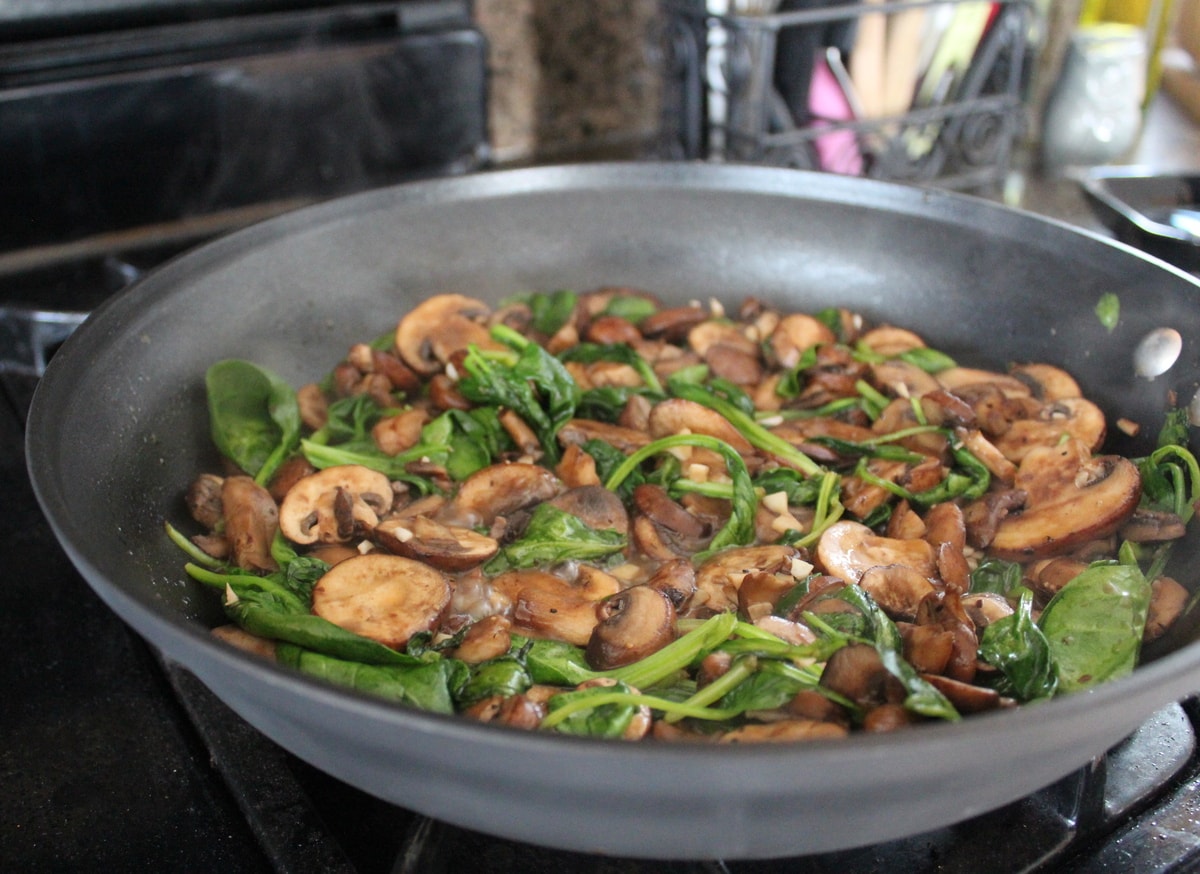 sliced mushrooms and fresh spinach leaves in a skillet on the stove