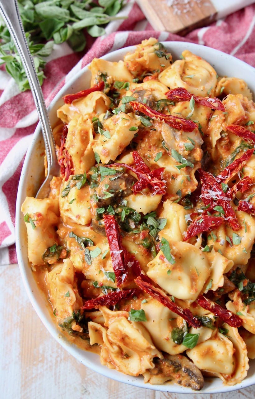 Pesto tortellini with sun dried tomatoes and fresh basil in bowl with spoon