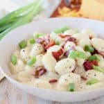 Gnocchi in cream sauce in bowl topped with bacon pieces and diced green onions