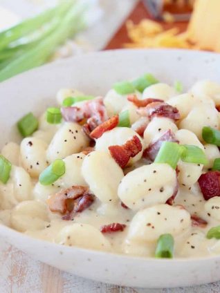 Gnocchi in cream sauce in bowl topped with bacon pieces and diced green onions