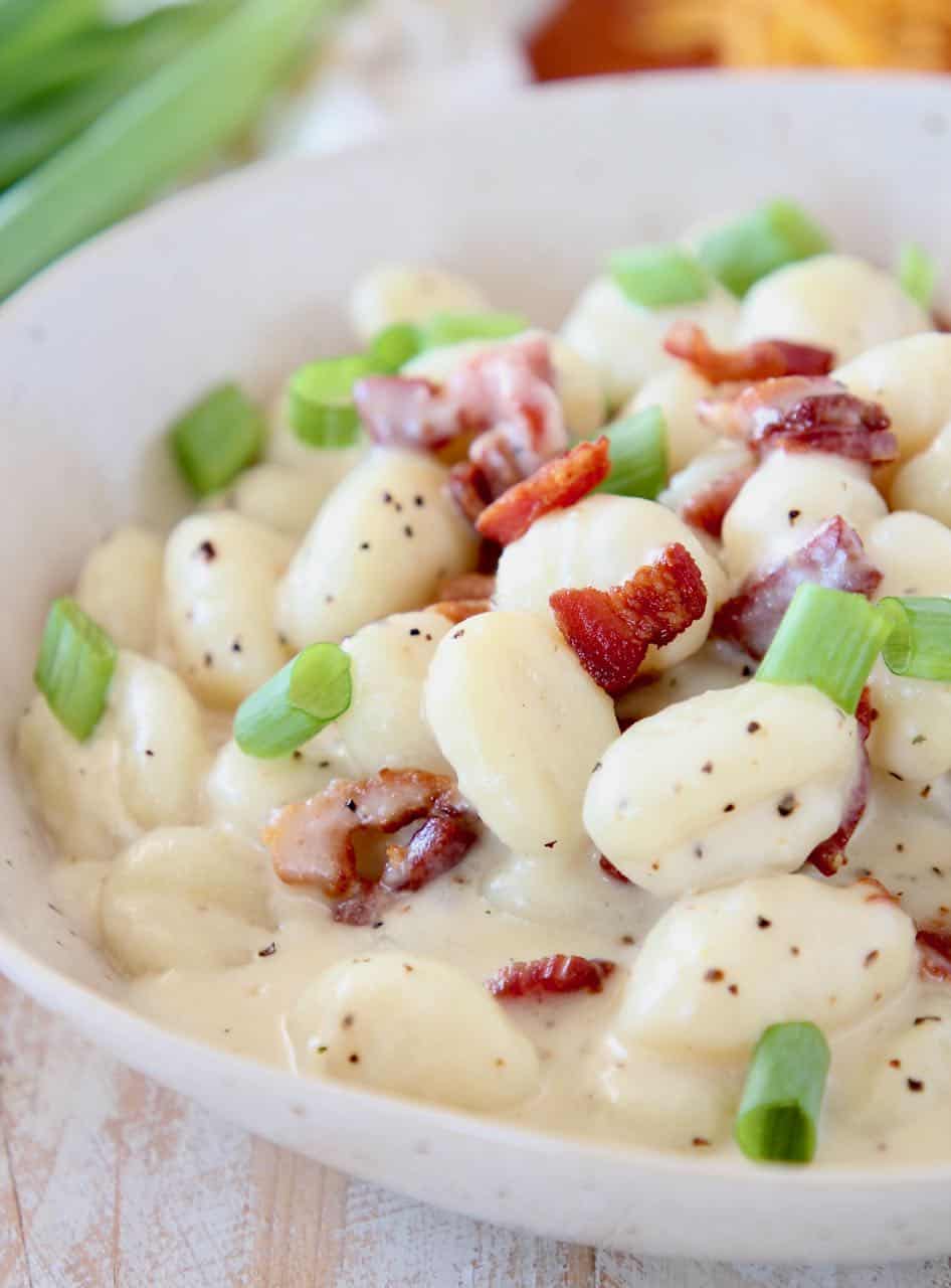 Potato gnocchi in bowl with creamy sauce, bacon pieces and diced green onions